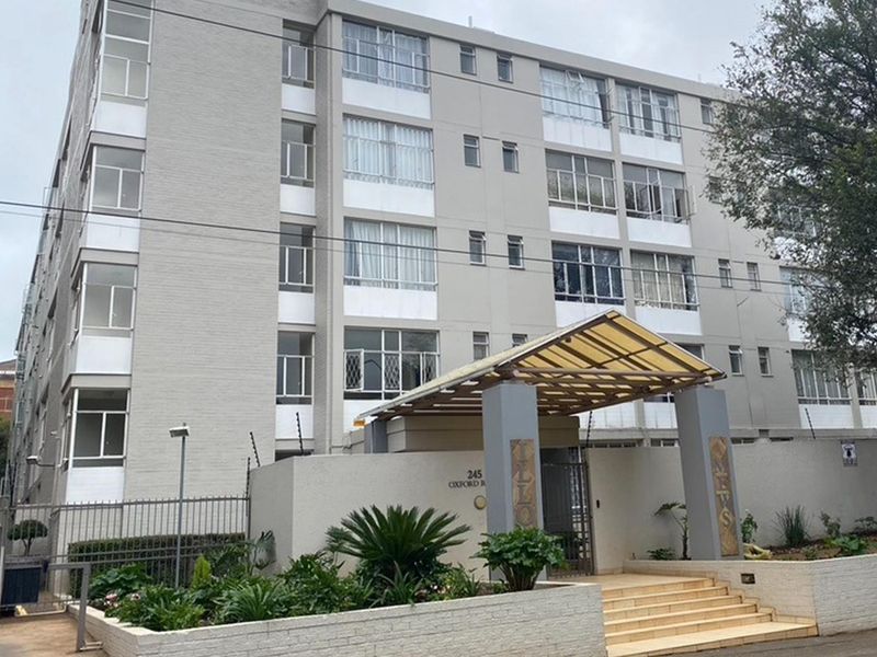 Front exterior view of a multi-story apartment building featuring a covered entrance, concrete stairs, and perimeter security fencing.