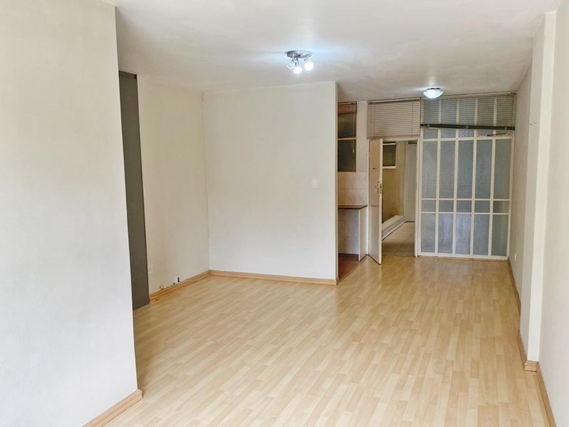 An empty living room featuring light-toned laminate flooring, neutral walls, and an internal glass panel door leading to an adjacent space.
