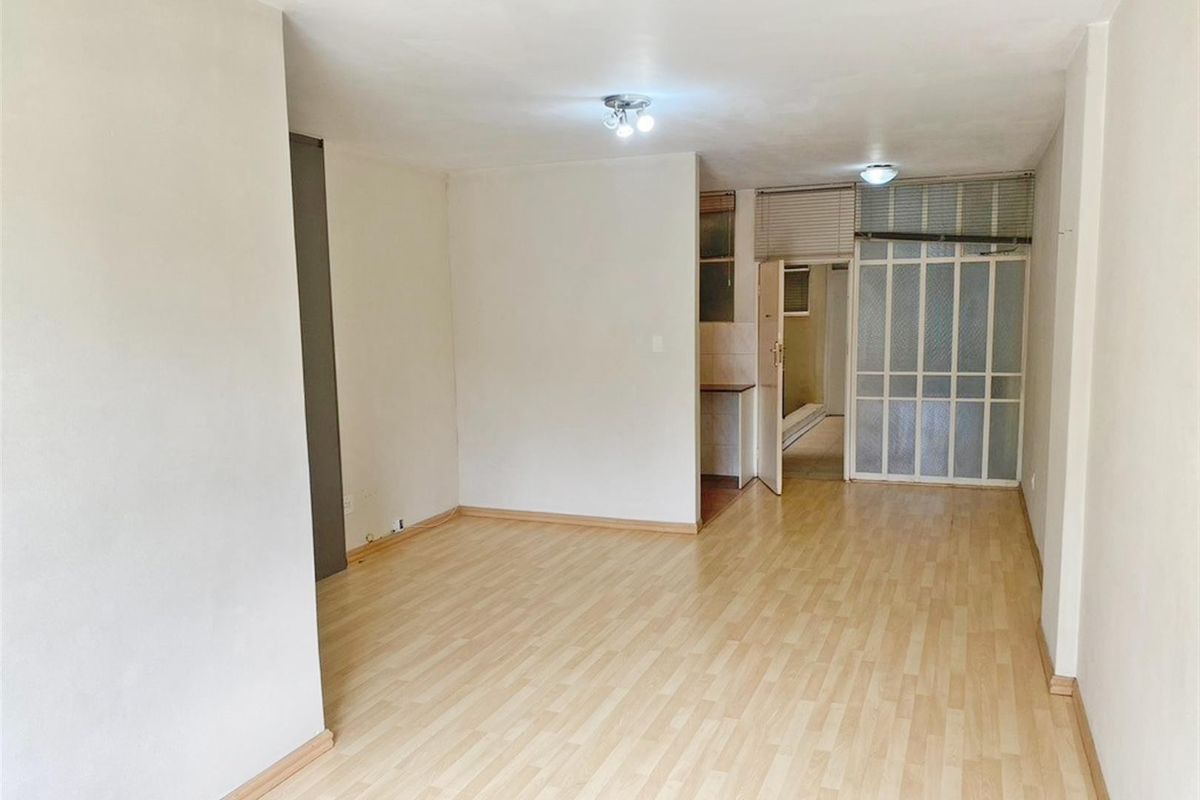 An empty living room featuring light-toned laminate flooring, neutral walls, and an internal glass panel door leading to an adjacent space.