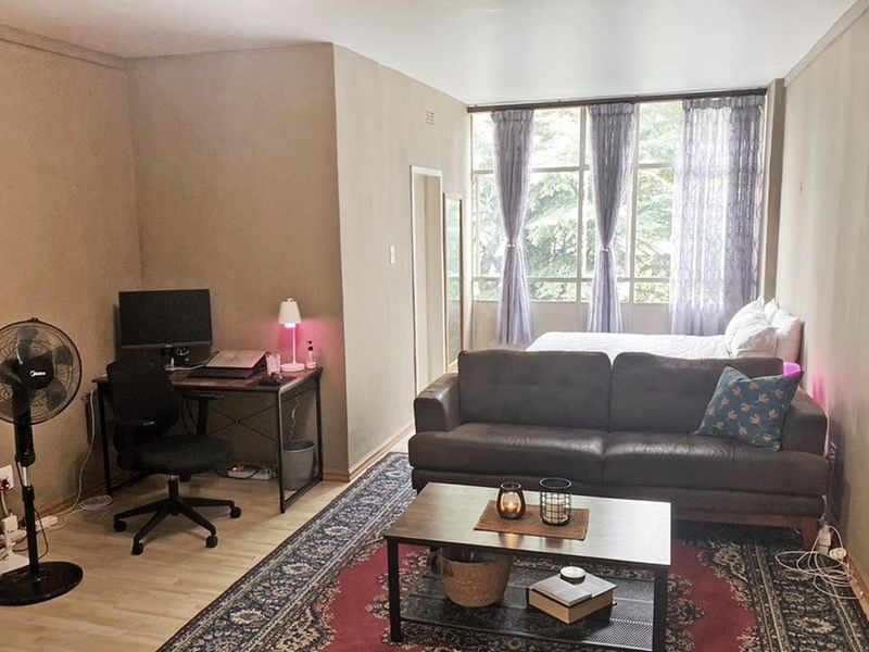 Open-plan living and sleeping area featuring large windows that provide natural light and laminate flooring throughout.