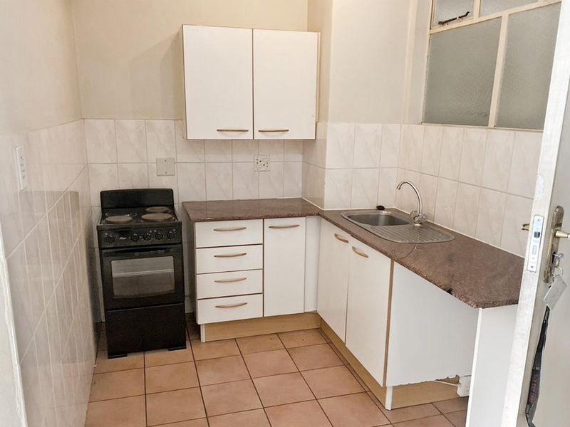 A compact kitchen featuring white cabinetry, granite countertops, a stainless steel sink, and a tiled backsplash, offering a functional layout for renovation.
