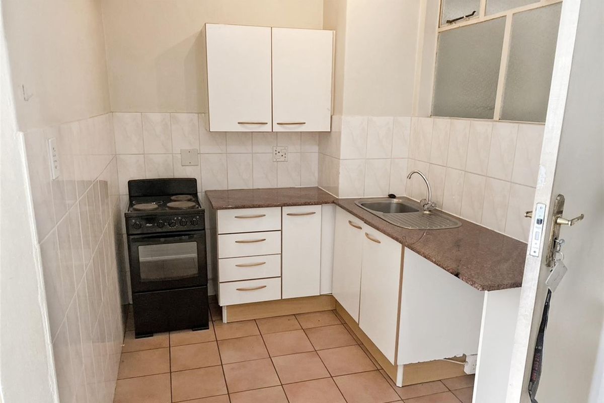 A compact kitchen featuring white cabinetry, granite countertops, a stainless steel sink, and a tiled backsplash, offering a functional layout for renovation.