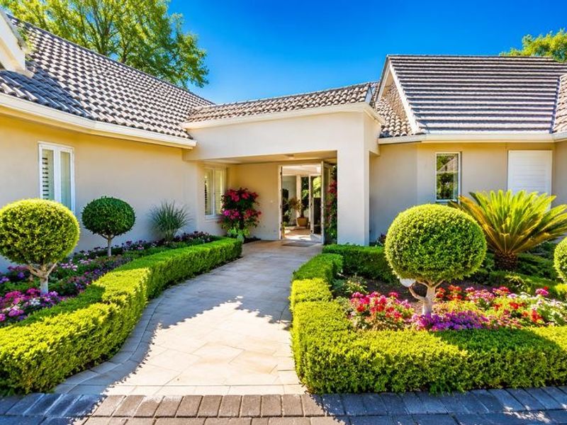 A well-maintained front entrance featuring a paved walkway, manicured hedges, and a covered porch area leading into the home.