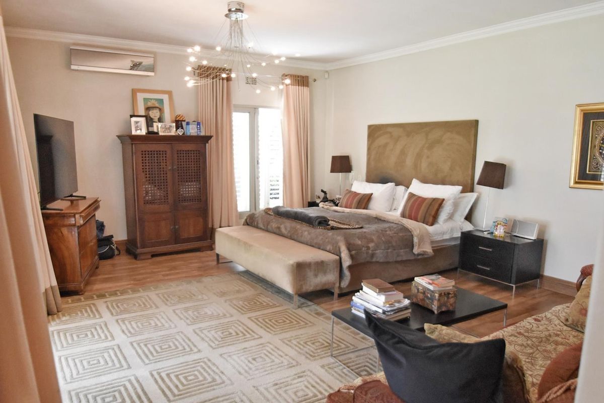Spacious bedroom featuring laminate flooring, crown molding, and a split-system air conditioner, with direct access to an outdoor area through sliding glass doors.
