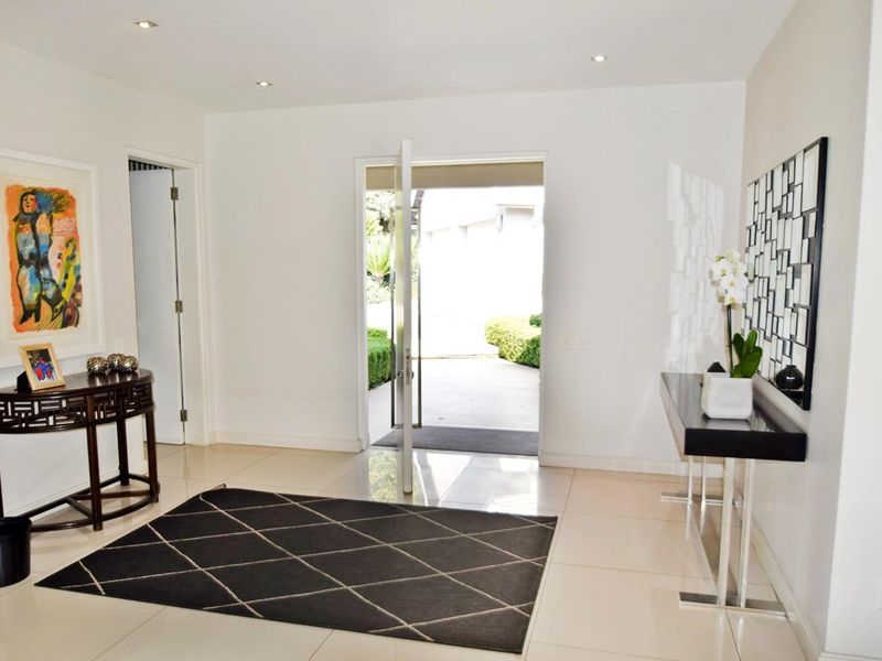 A bright and welcoming entrance hall featuring polished tiled flooring, recessed downlighting, and a modern pivot front door leading to the exterior.