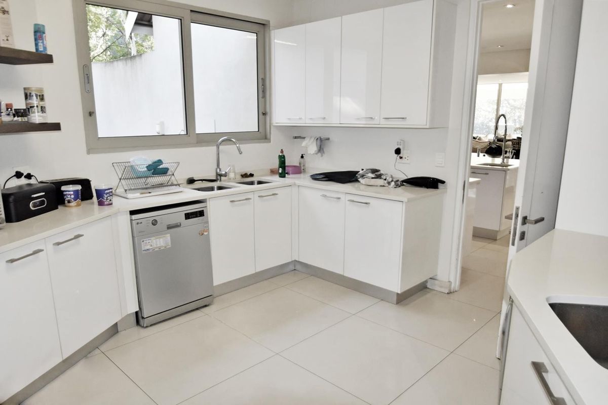 A modern kitchen featuring white cabinetry, stone countertops, a double sink, and tiled flooring, with an integrated dishwasher and clean finishes.
