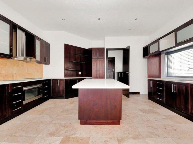 Spacious kitchen featuring dark wood cabinetry, a central island with stone countertops, built-in oven, extractor fan, and neutral tiled flooring.