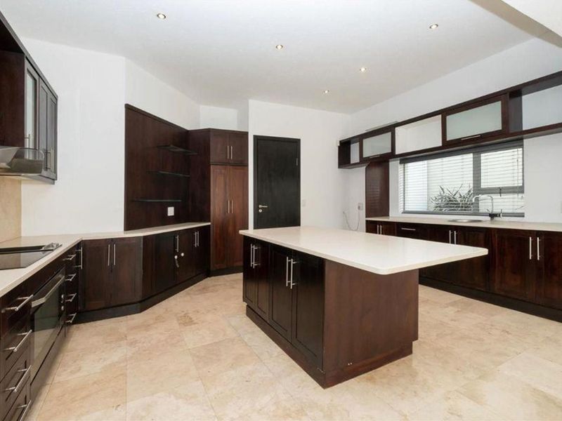 Spacious kitchen featuring dark wood cabinetry, stone countertops, a central island, and stone floor tiles, offering a clean and functional layout.