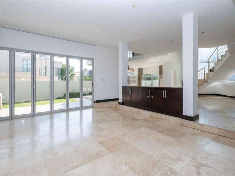 Spacious open-plan living area featuring polished travertine floors, modern bi-fold doors leading to the garden, and a sleek staircase with glass balustrades.