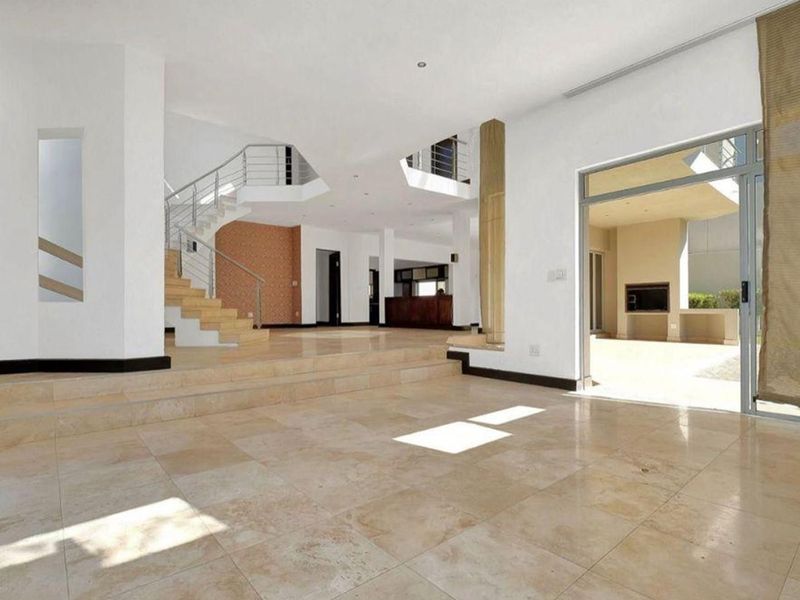 Spacious open-plan living area featuring stone tile flooring, a modern staircase with metal balustrades, and seamless access to an outdoor patio area.