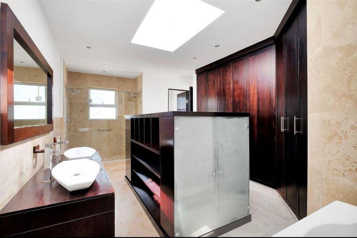 Spacious modern bathroom featuring a double vanity with vessel sinks, extensive built-in cabinetry, a walk-in shower, and a large skylight for natural illumination.