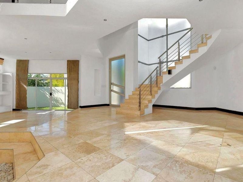 Spacious open-plan living area featuring polished travertine flooring, a modern staircase with stainless steel railings, and abundant natural light from a large skylight.