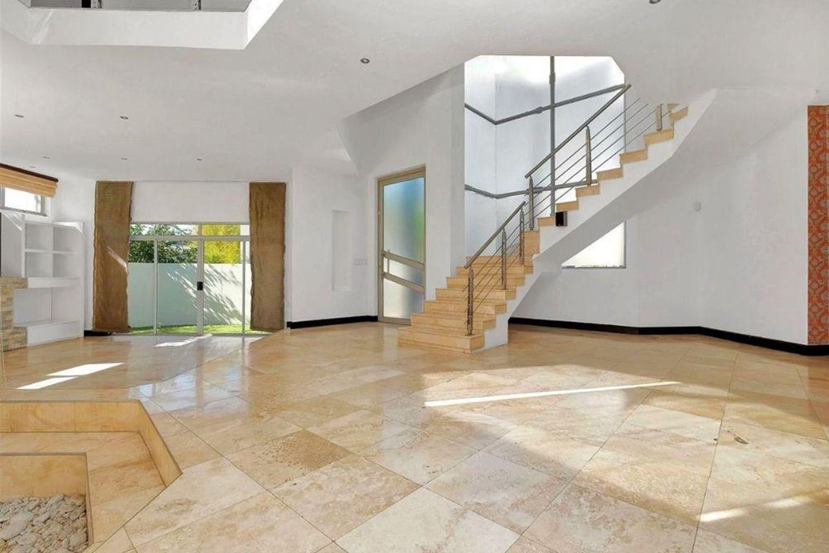Spacious open-plan living area featuring polished travertine flooring, a modern staircase with stainless steel railings, and abundant natural light from a large skylight.