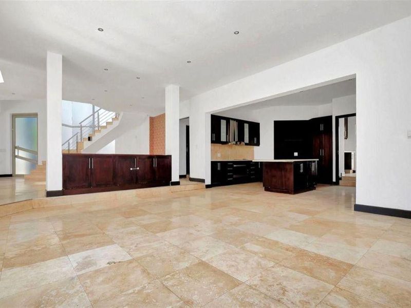 Spacious open-plan living area featuring travertine flooring, a modern kitchen with dark cabinetry, and a central staircase leading to the upper level.