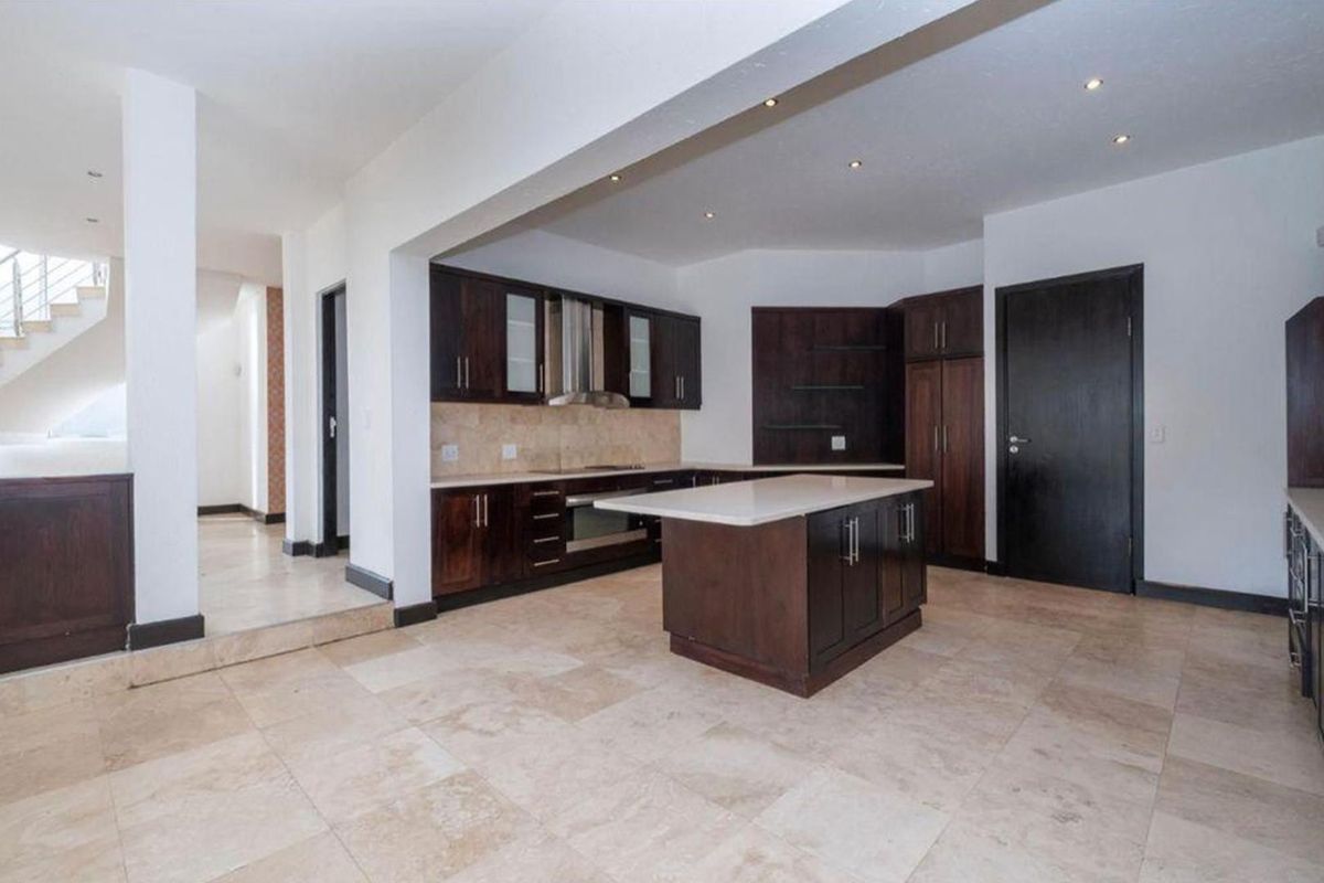 Spacious open-plan kitchen featuring dark wood cabinetry, a central island with stone countertops, and neutral tiled flooring throughout.