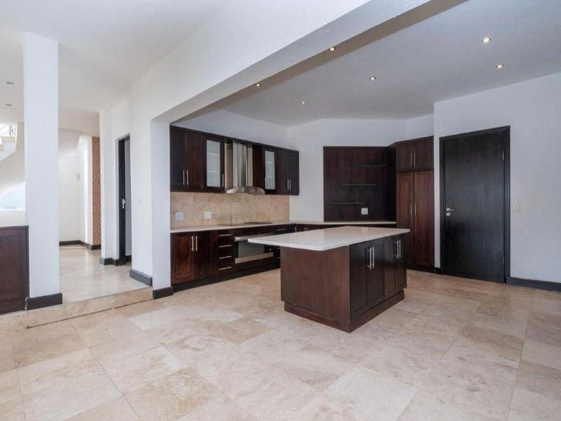 Spacious open-plan kitchen featuring dark wood cabinetry, a central island with stone countertops, and neutral tiled flooring throughout.