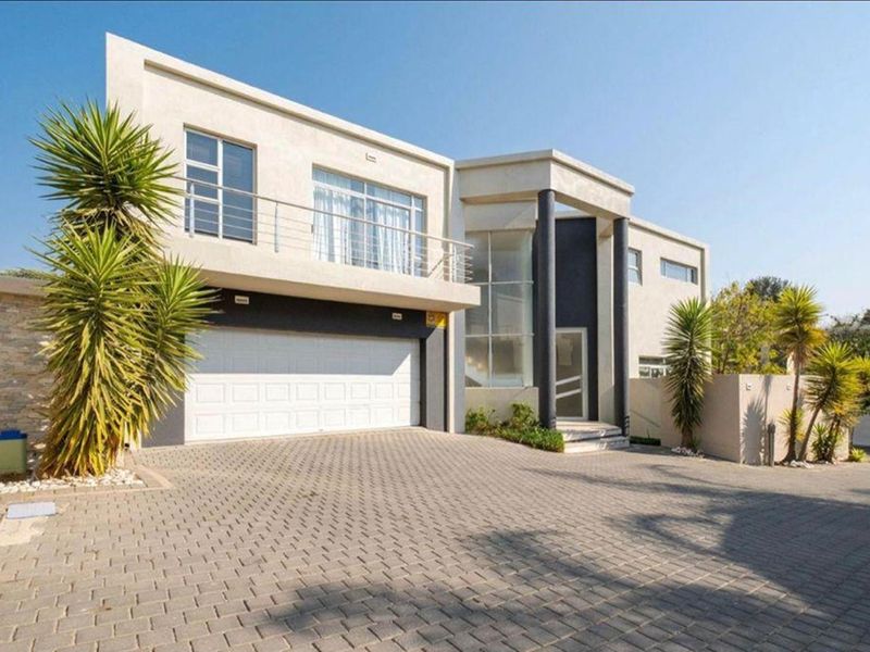 Modern double-story residence featuring a paved driveway, double garage, and a prominent entrance with stone cladding and a balcony.