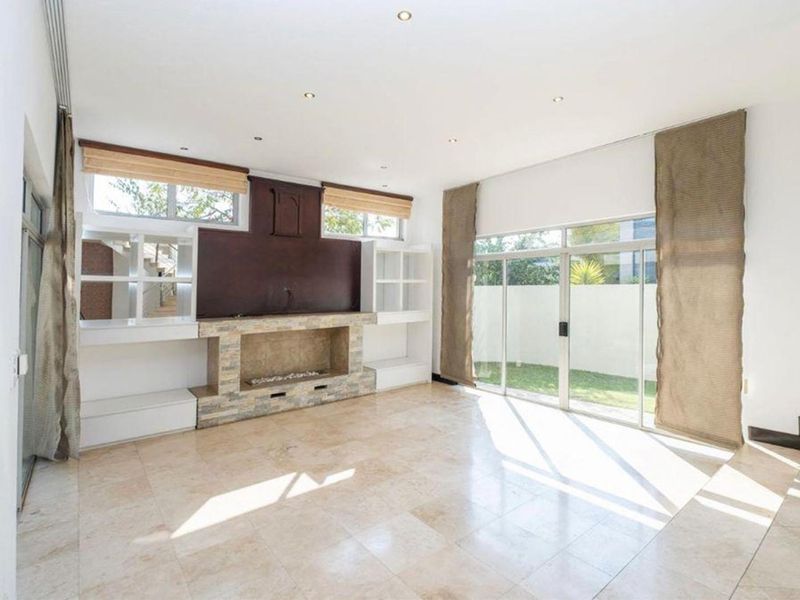 Spacious living room featuring marble tile flooring, a stone-clad fireplace with built-in shelving, and large sliding glass doors opening to the garden.
