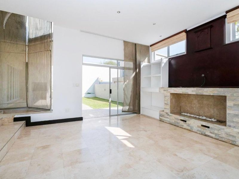 Spacious living room featuring travertine tile flooring, a stone-clad fireplace, built-in shelving, and direct access to the rear garden through a sliding glass door.