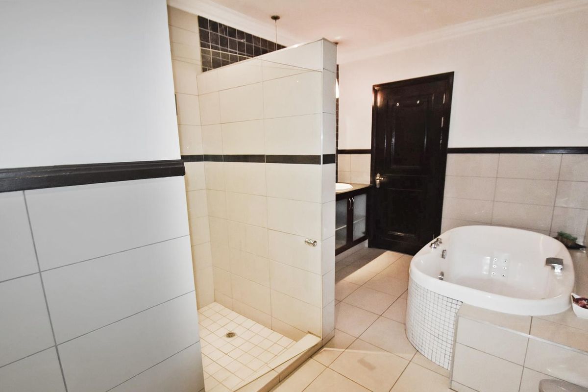 A spacious bathroom featuring a walk-in shower, a built-in bathtub, and a vanity cabinet with neutral wall and floor tiling.