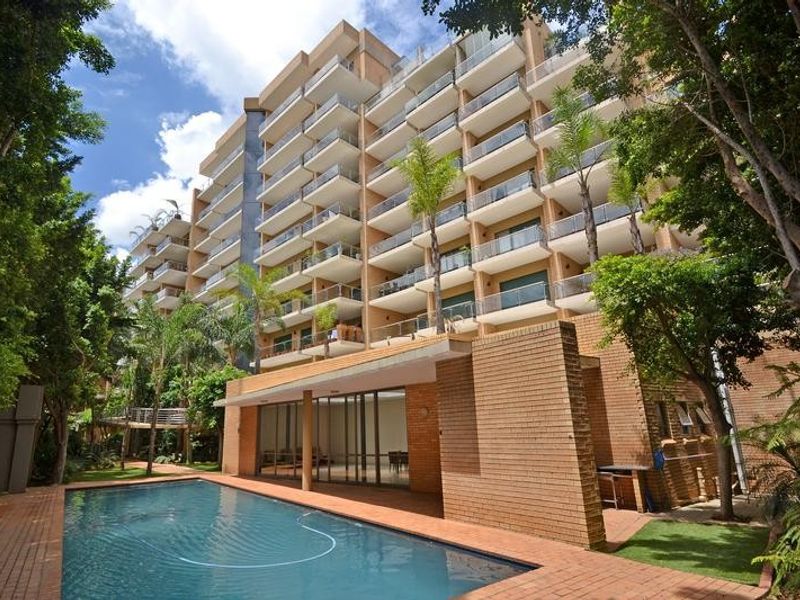 A well-maintained apartment complex featuring a swimming pool, brick-paved patio area, and multiple levels of balconies with glass balustrades.