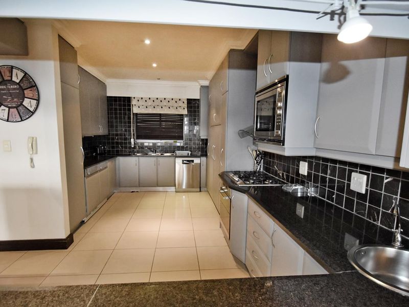 Modern kitchen featuring grey cabinetry, granite countertops, gas hob, built-in oven, microwave, and tiled finishes throughout.