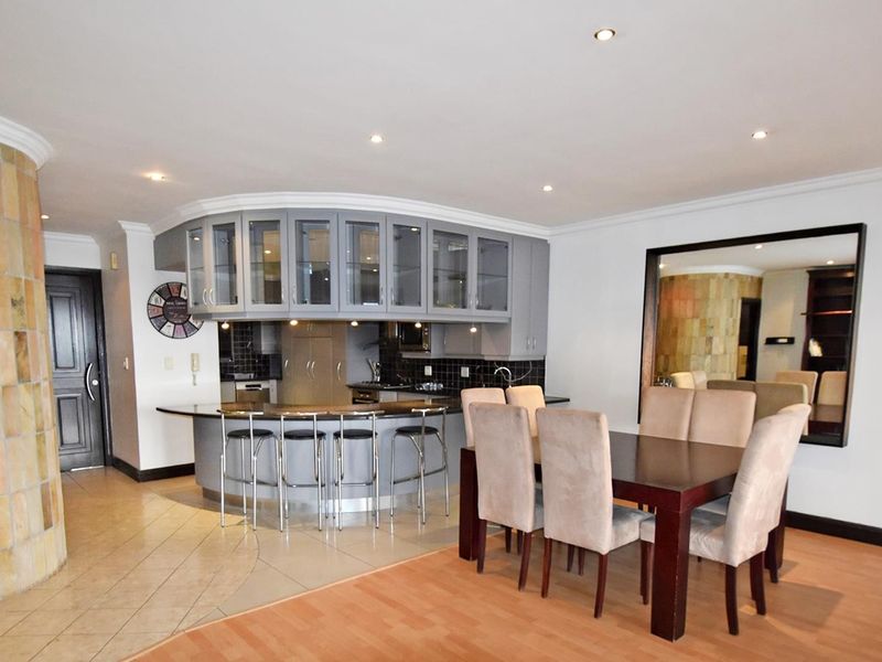 Open-plan living and dining area featuring a unique curved kitchen island with glass-fronted cabinetry, stone-clad pillar, and modern recessed lighting.