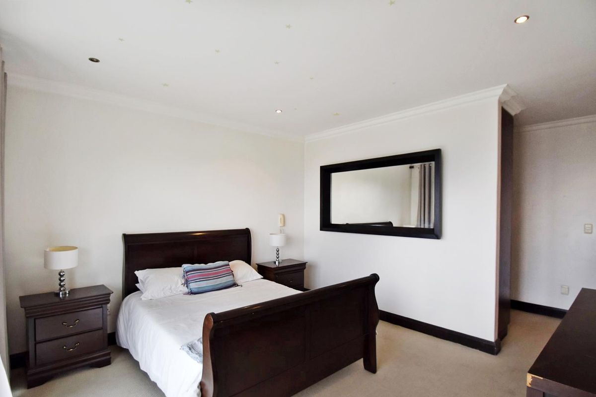 A well-maintained bedroom featuring recessed downlighting, decorative coving, and a large wall-mounted mirror, finished with neutral carpeting.