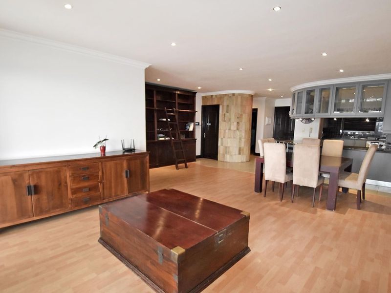 Spacious open-plan living and dining area featuring laminate flooring, recessed lighting, a stone-clad feature pillar, and integrated kitchen cabinetry with stone countertops.