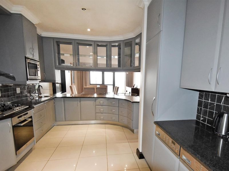 Modern kitchen featuring grey cabinetry, granite countertops, integrated appliances, and a curved layout that flows into the adjacent dining area.