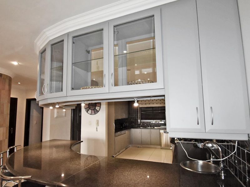 A modern kitchen featuring a distinctive curved granite breakfast bar, glass-fronted cabinetry, and elegant under-cabinet lighting, creating a functional and stylish culinary space.
