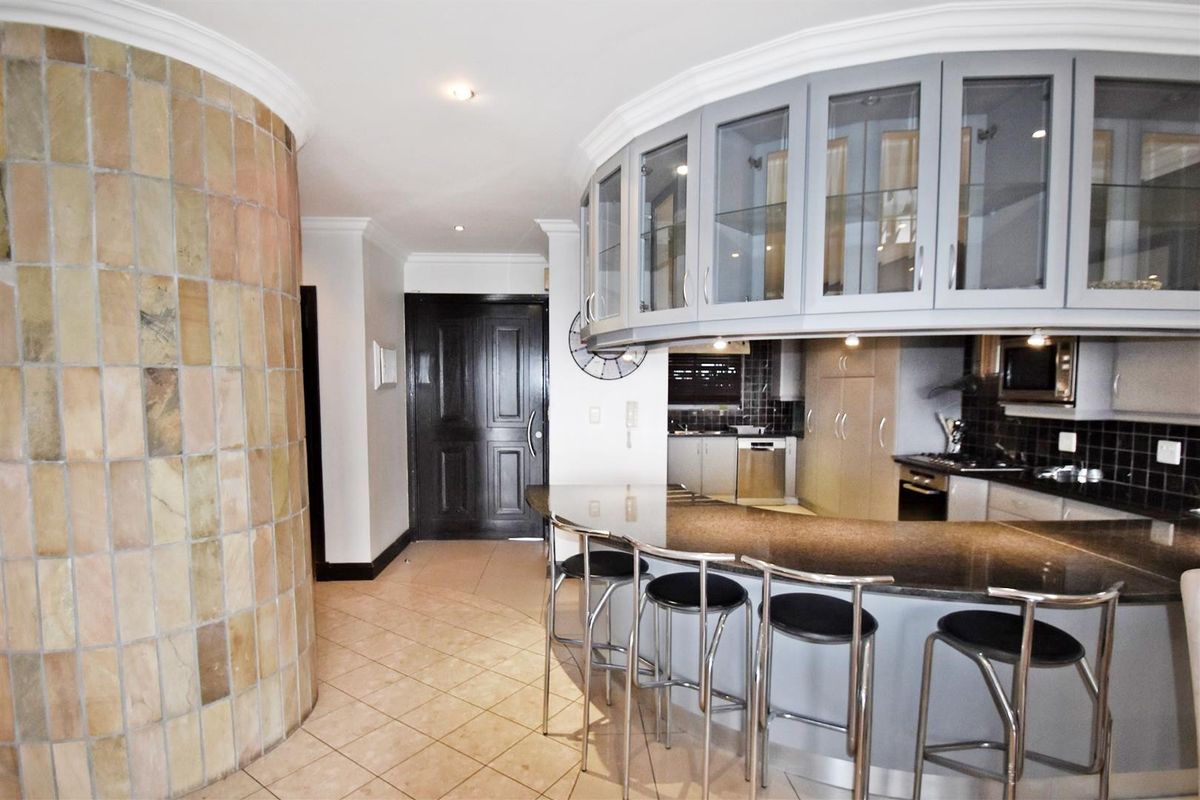 A modern kitchen featuring a unique curved island with granite countertops, glass-fronted cabinetry, and integrated appliances, complemented by a distinctive tiled feature wall.
