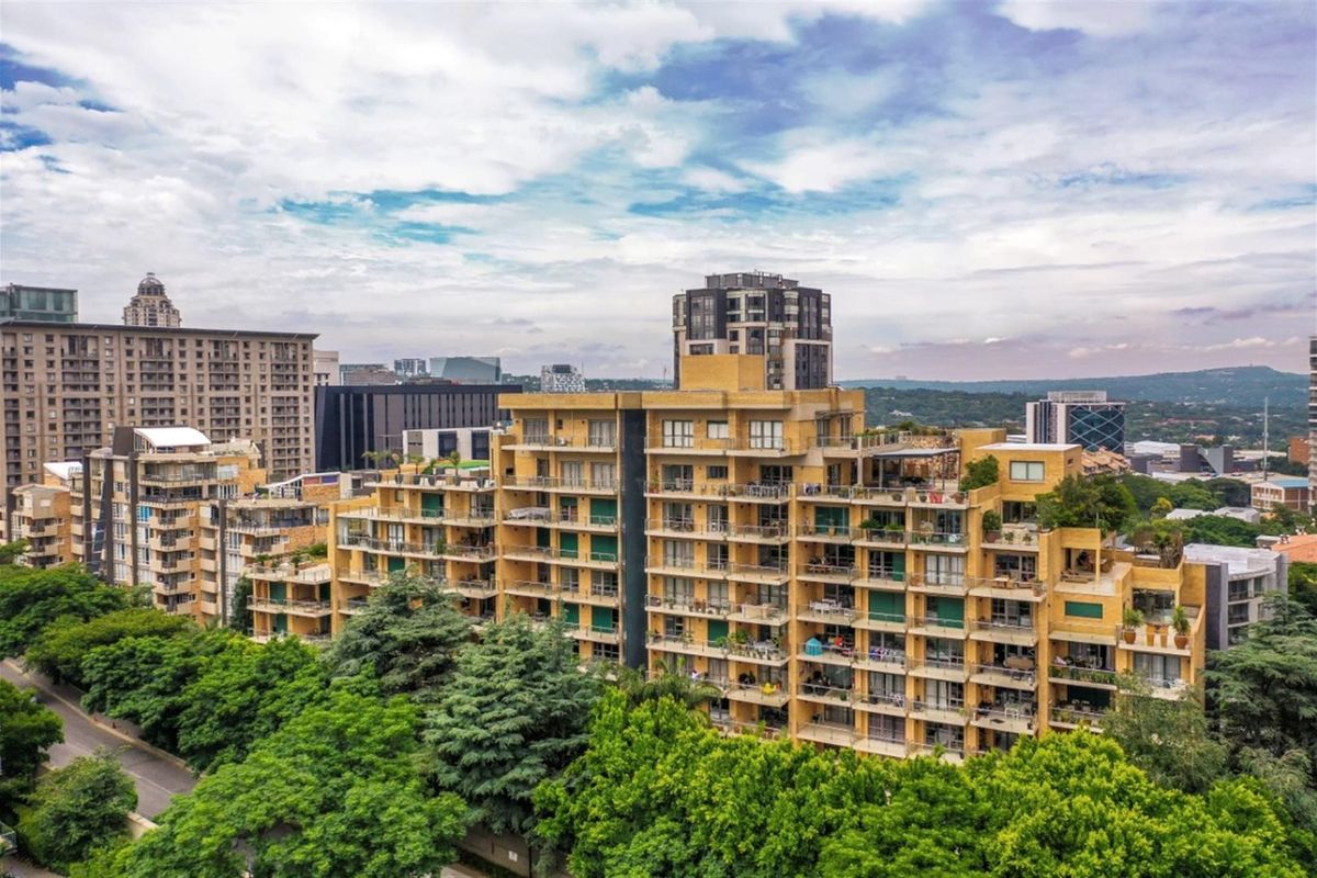 Aerial view of a multi-story apartment complex featuring tiered balconies and terraces set within a landscaped urban environment.