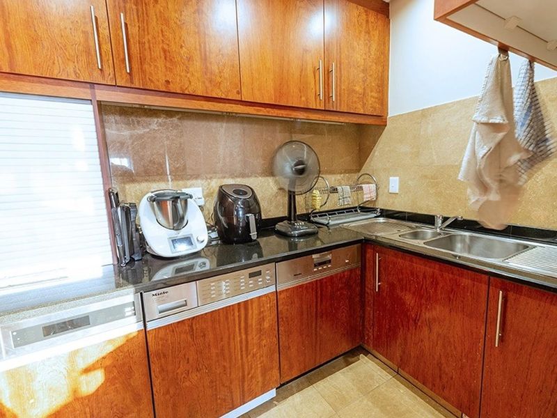 A functional kitchen featuring warm-toned wooden cabinetry, granite countertops, a stainless steel double sink, and integrated dishwasher, finished with a tiled backsplash.