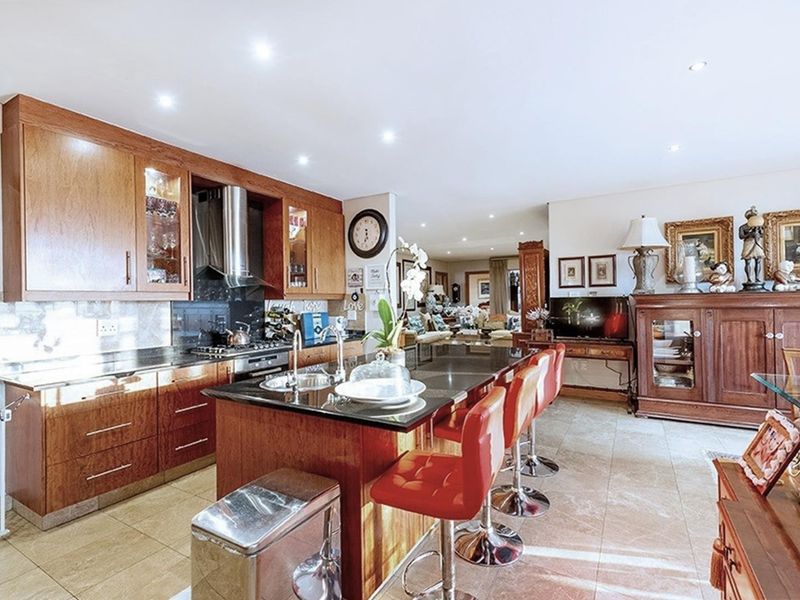 Spacious open-plan kitchen featuring warm wood cabinetry, granite countertops, a central island with breakfast bar seating, and integrated stainless steel appliances.