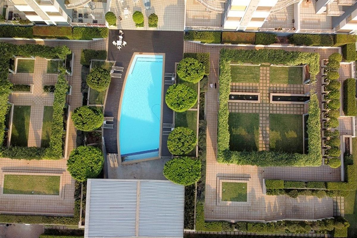Aerial view of a well-maintained apartment complex featuring a swimming pool, landscaped gardens, and paved outdoor recreational areas.