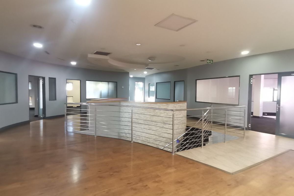 Spacious office hallway featuring modern laminate flooring, a central staircase with stainless steel balustrade, and stone-clad architectural detailing.