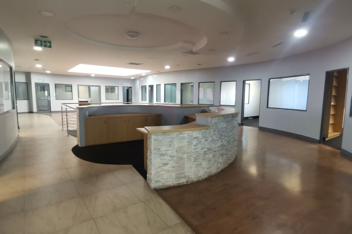 Spacious office reception area featuring a curved stone-clad built-in desk, recessed ceiling lighting, and multiple glass-partitioned office rooms.