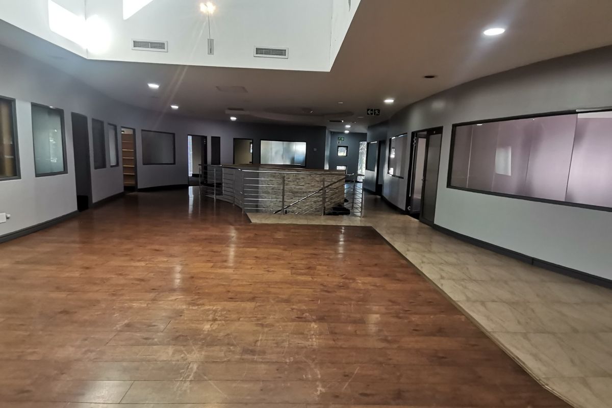 Spacious open-plan office area featuring a mix of laminate and tiled flooring, recessed lighting, a central skylight, and modern glass partitions.