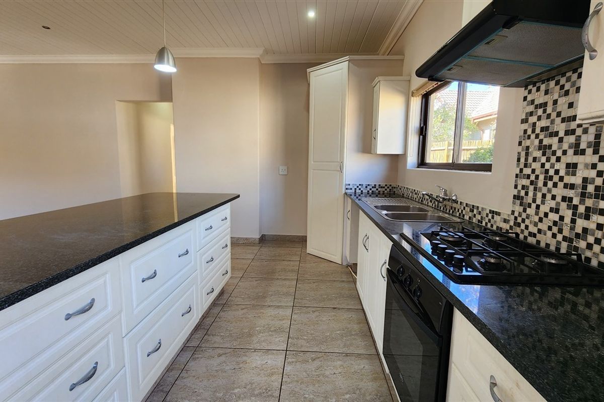 A functional kitchen featuring white cabinetry, granite countertops, a gas hob with extractor, and a mosaic tile backsplash, offering a clean and practical workspace.