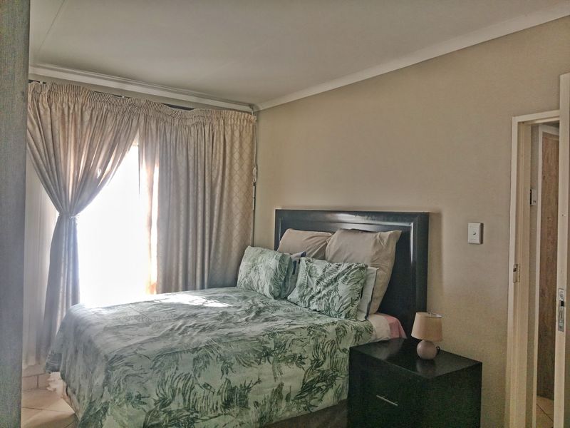 A functional bedroom featuring neutral wall tones, natural light through window curtains, and a doorway leading to an adjacent space.
