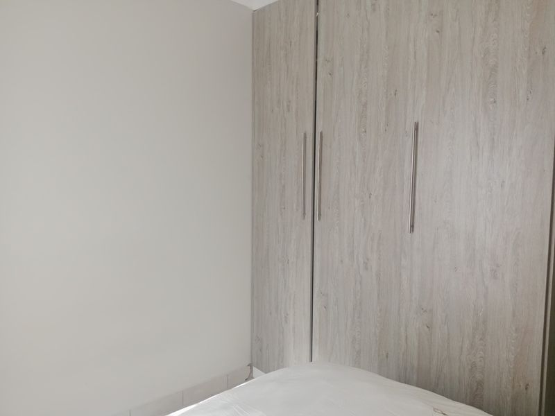 A bedroom featuring modern, light wood-grain built-in cupboards with sleek metal handles.