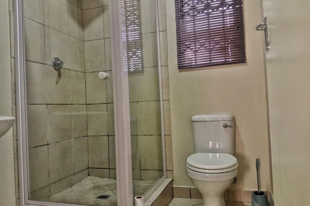 A compact bathroom featuring a shower enclosure with tiled walls and a standard toilet, requiring some maintenance to the grout and finishes.