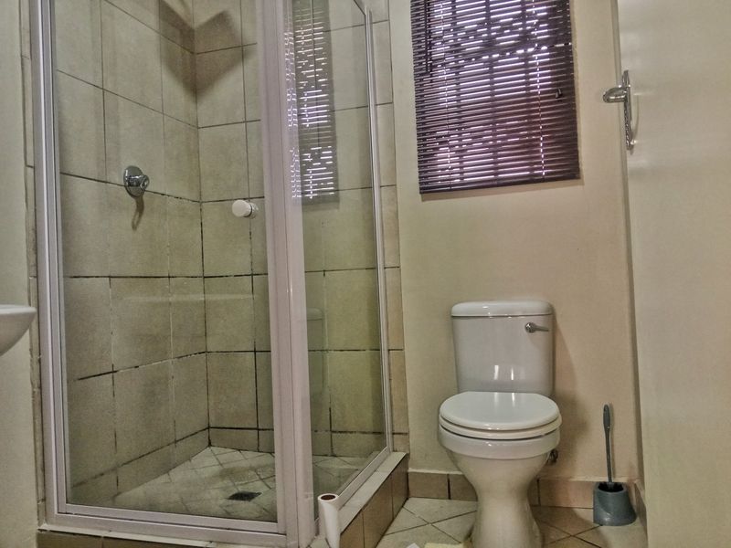 A compact bathroom featuring a shower enclosure with tiled walls and a standard toilet, requiring some maintenance to the grout and finishes.