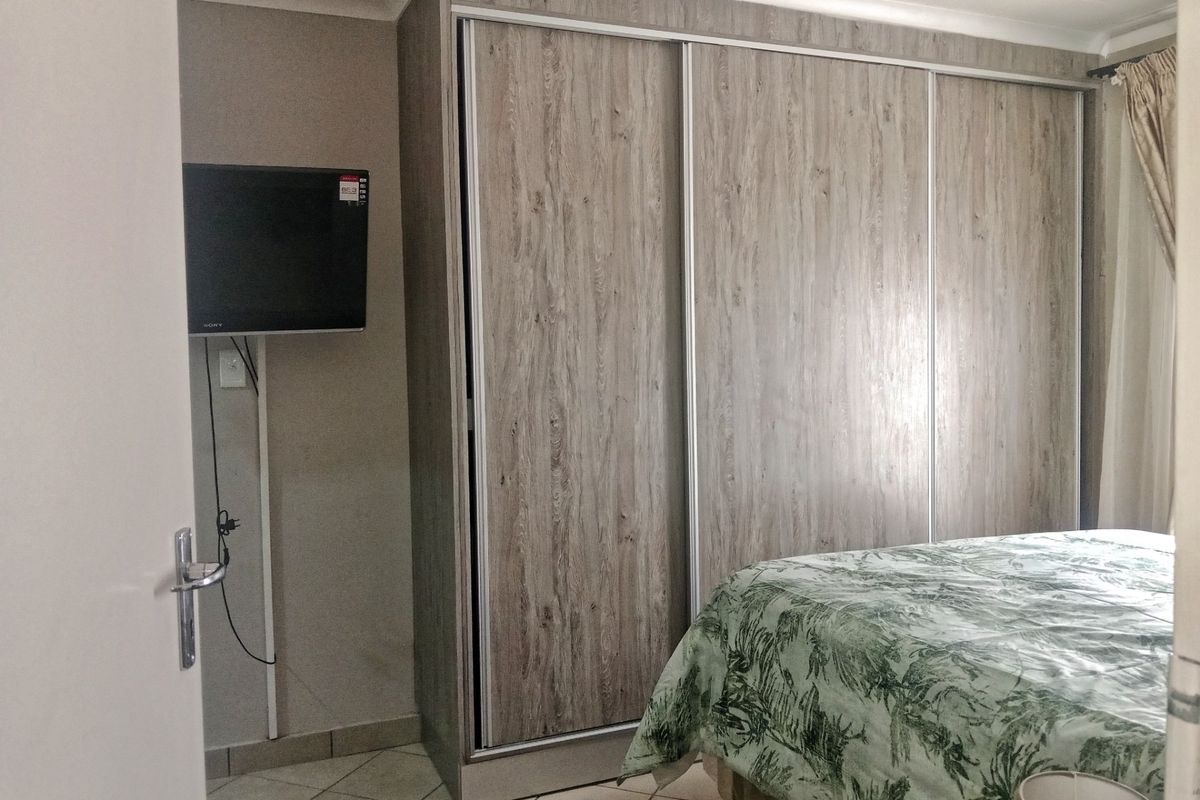 A bedroom featuring light wood-grain built-in sliding door wardrobes and tiled flooring.