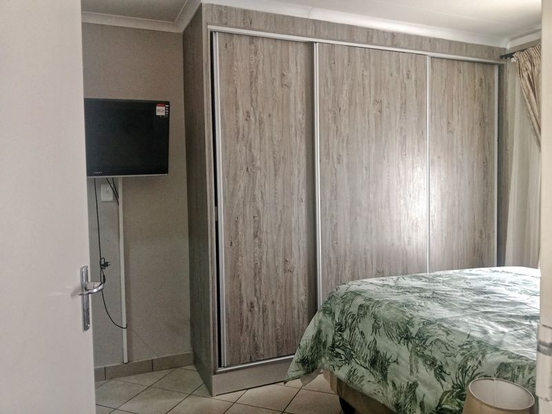 A bedroom featuring light wood-grain built-in sliding door wardrobes and tiled flooring.