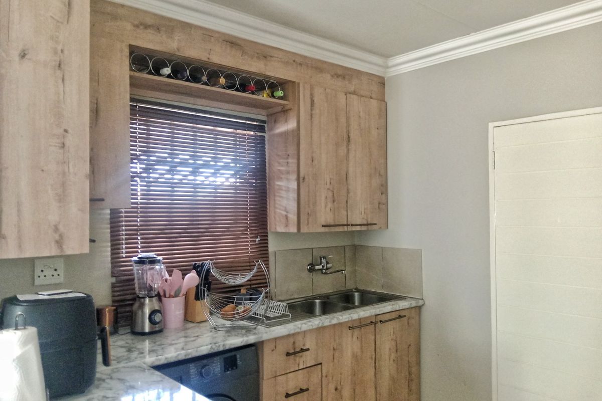 A functional kitchen featuring wood-look cabinetry, marble-effect countertops, a double stainless steel sink, and integrated wine storage with neutral wall finishes.