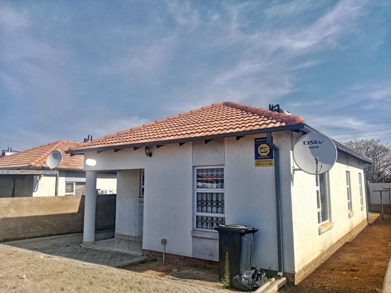 Front elevation of a single-story residential house featuring a tiled roof, paved entrance area, and security window bars.