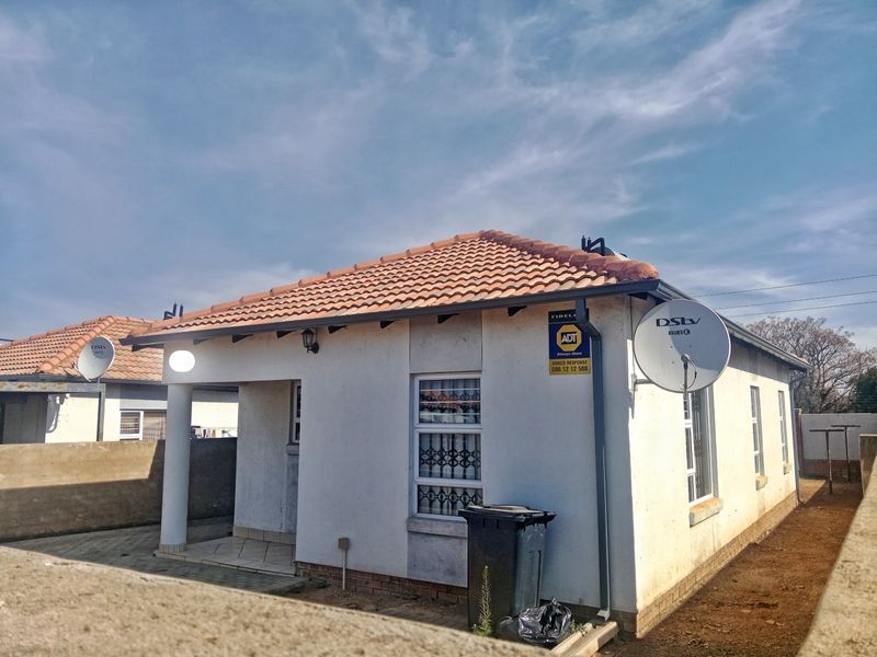Front view of a single-story residential house featuring a tiled roof, security bars on windows, and a paved entrance area.