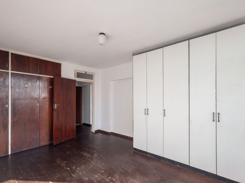 Spacious bedroom featuring extensive built-in cupboard storage and original wooden flooring, offering a blank canvas for renovation and modernization.